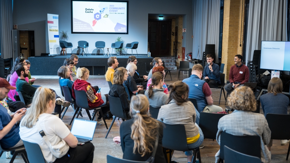 Workshopteilnehmer*innen sitzen auf ihren Stühlen und hören den Workshopleitern zu.