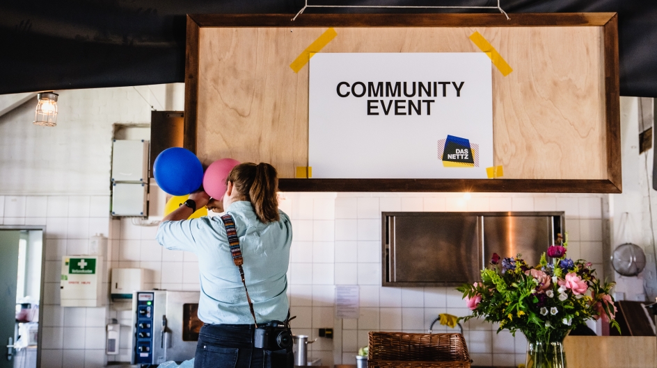 Frau befestigt drei Luftballons an einem Schild, auf dem "Community Event" steht